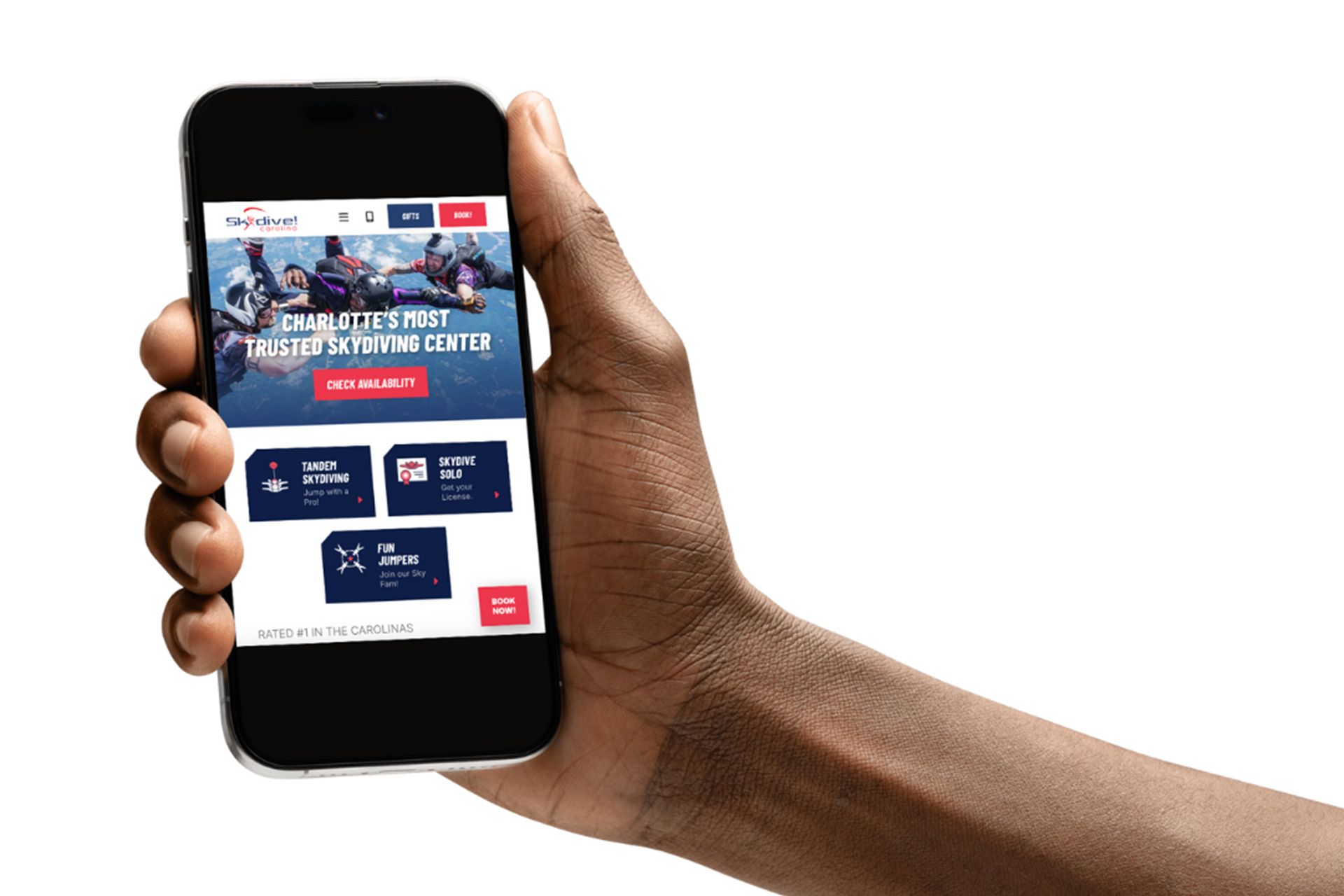 A hand holding a smartphone displaying a skydiving center’s website, with images of skydivers, booking options, and bold text reading "Charlotte’s Most Trusted Skydiving Center.